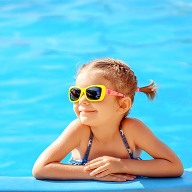 Un copil mic zâmbeşte la marginea unei piscine. Duritatea apei în piscine poate deteriora suprafeţele piscinei şi coroda conductele.